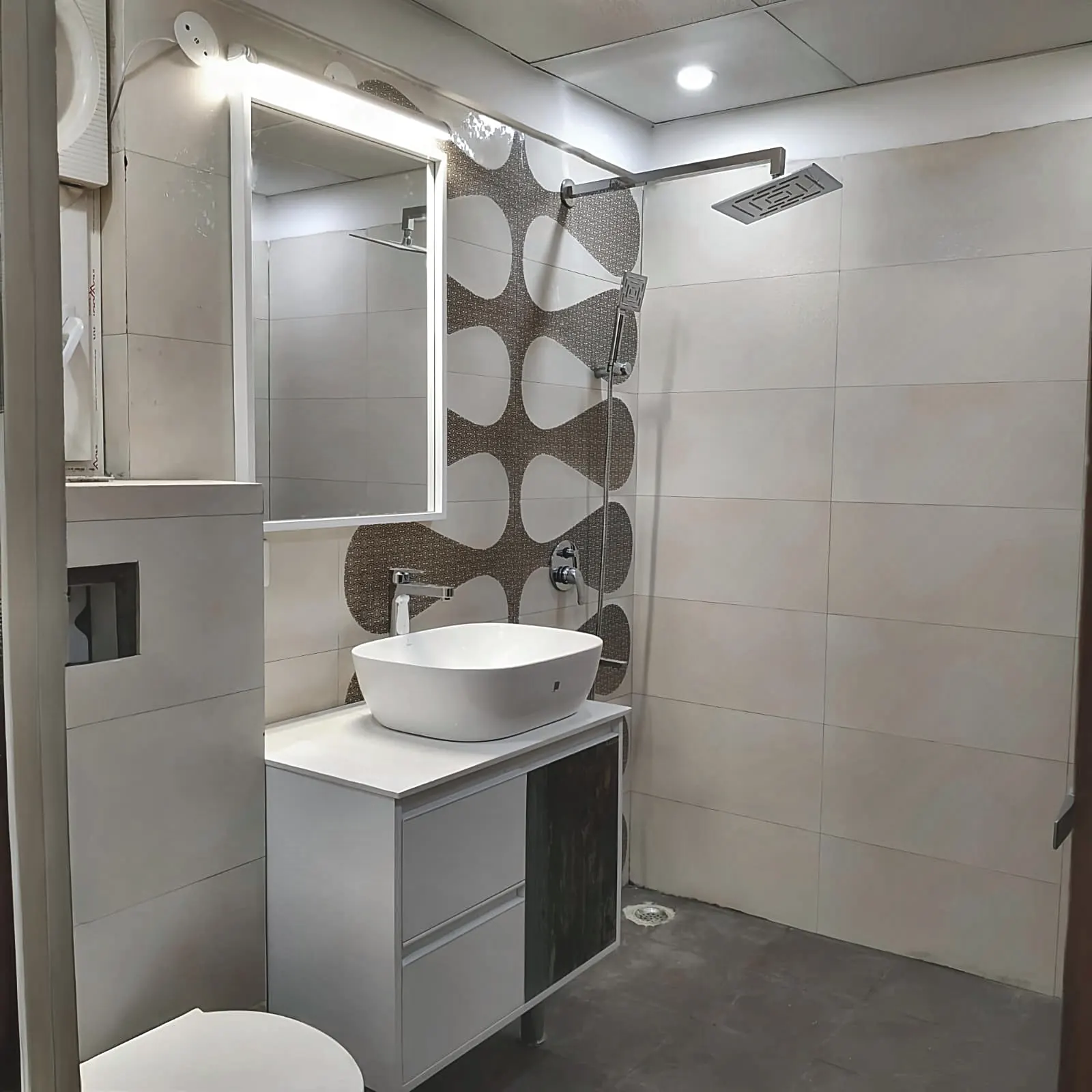 Bathroom vanity by Livibi with an LED-backlit oval mirror, geometric brown-and-white accent tile, and rain shower head