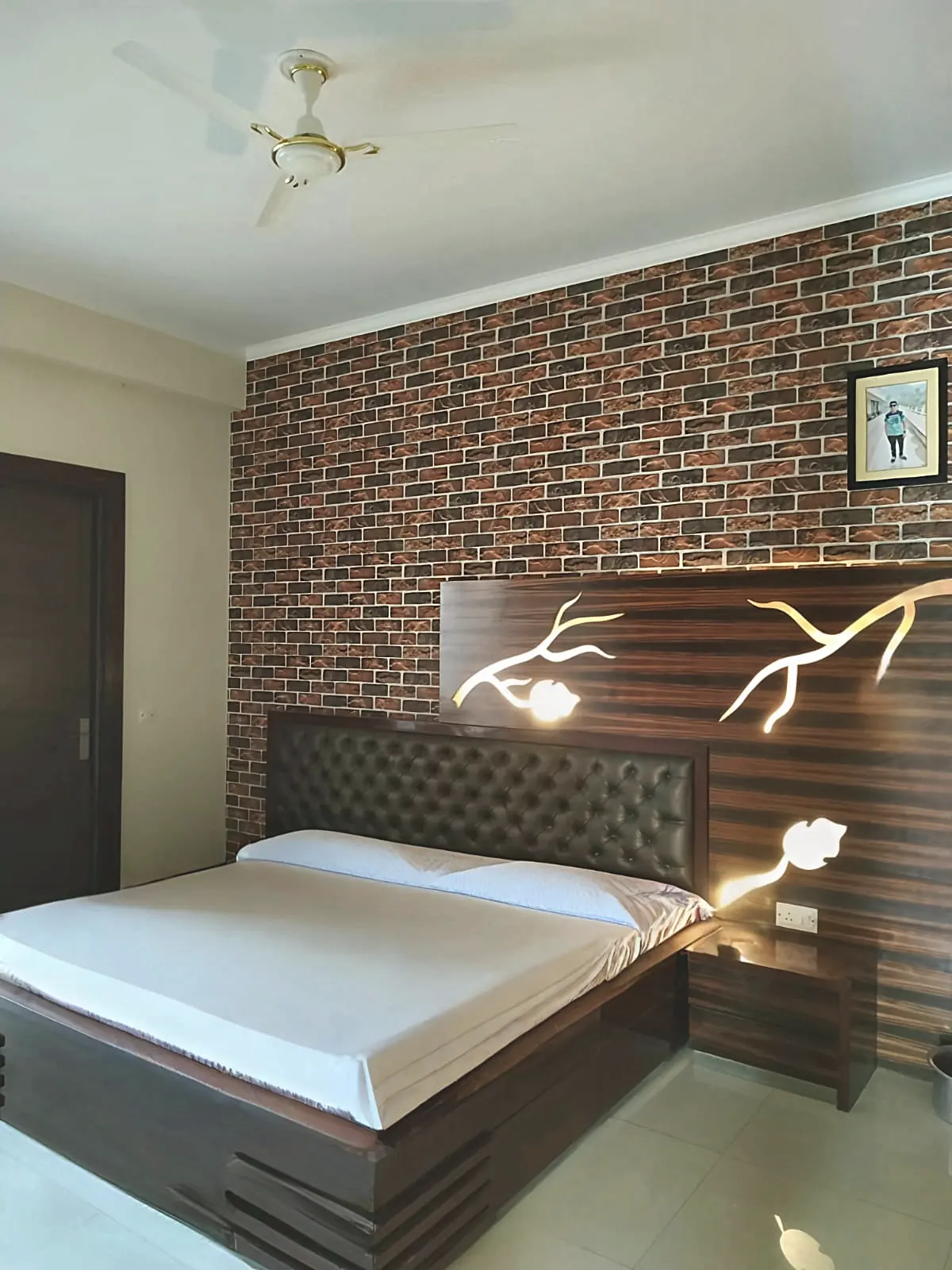 Bedroom with a rustic brick-effect wallpaper accent wall and a dark wood headboard featuring an illuminated carved-branch motif