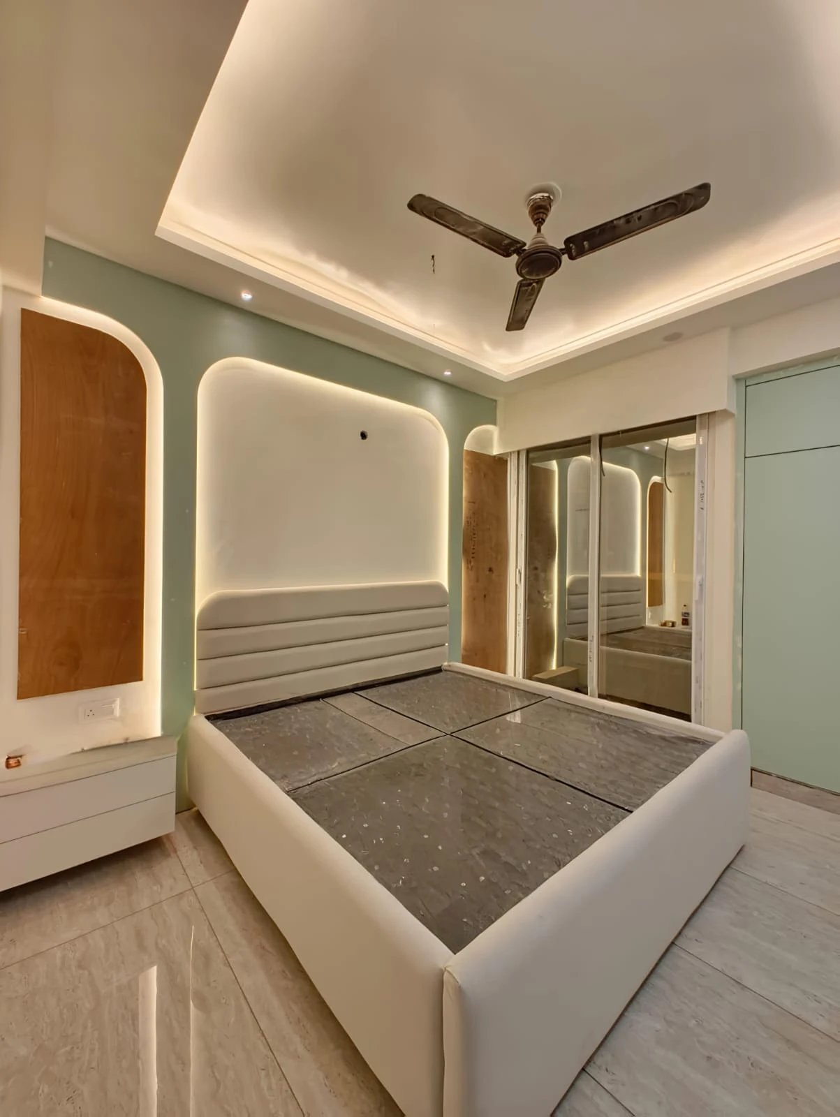 Sage-green bedroom with an arched, channel-tufted white headboard set into a backlit alcove