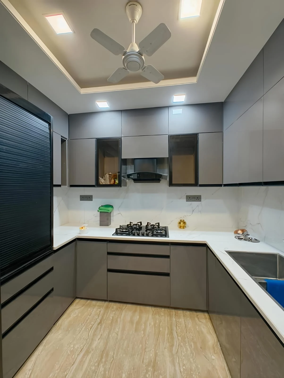 Grey U-shaped modular kitchen by Livibi with a black hob, textured-panel refrigerator and a barred window