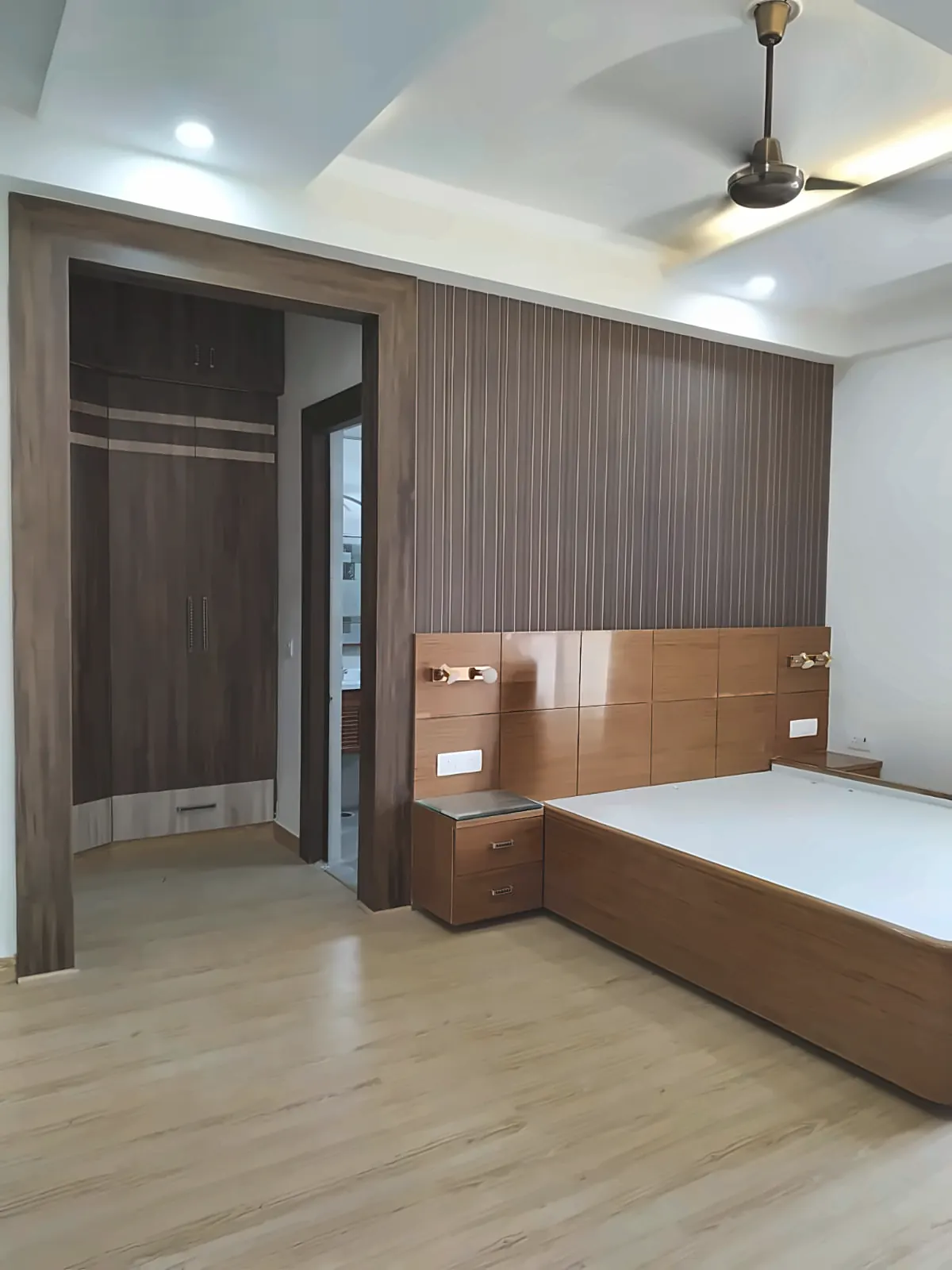 Bedroom corner with an open dark-wood wardrobe showing a hanging rod, shelf and drawer front