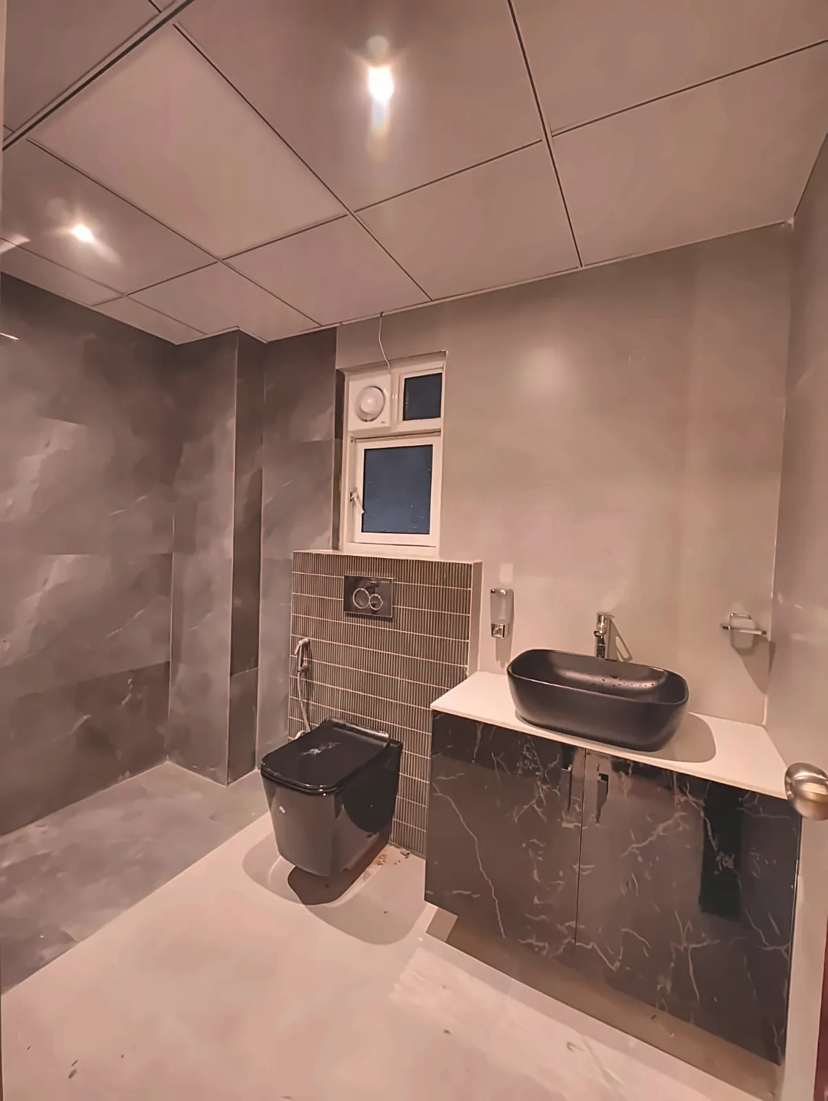 Wet-room-style bathroom by Livibi with a wall-hung black toilet and cistern, wall-mounted health spray, and drop ceiling
